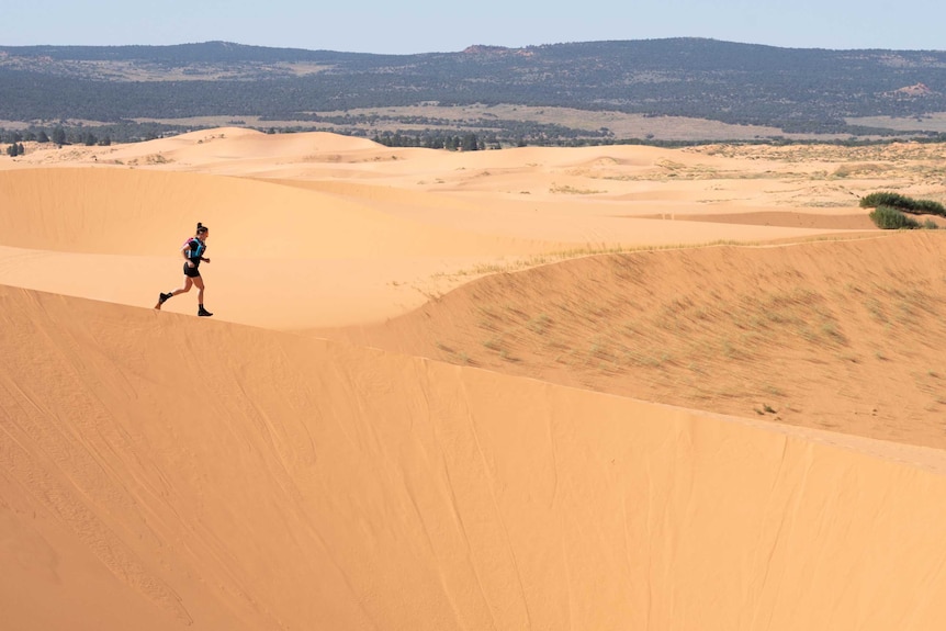 An athlete runs through sand dunes in the Grand Canyon region of the USA.