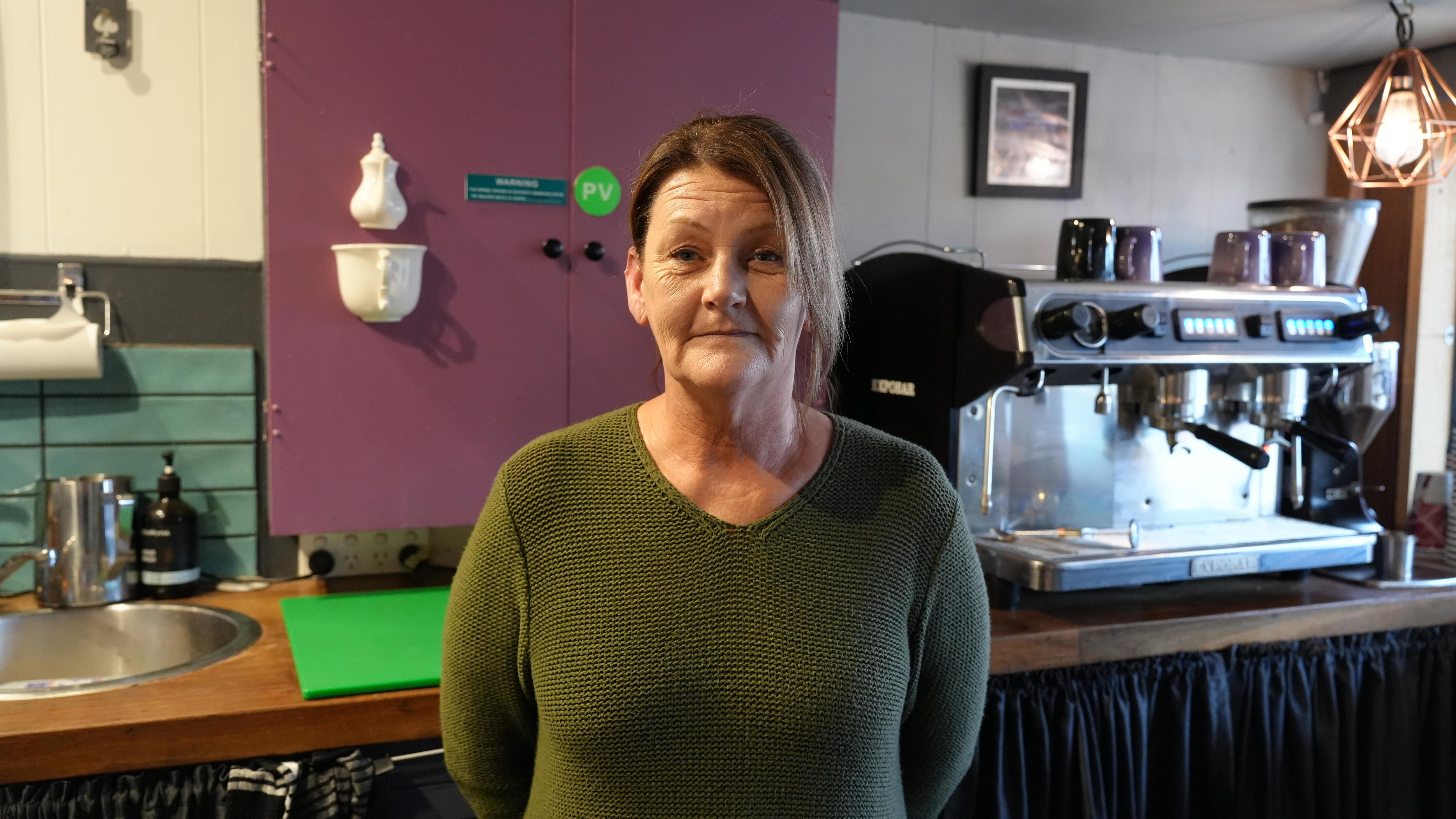 A woman in a cafe stands behind the counter near her coffee machine.