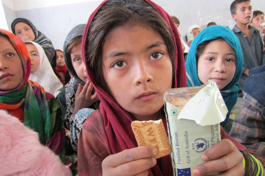Girl wearing headscarf holding biscuits from Australian government.