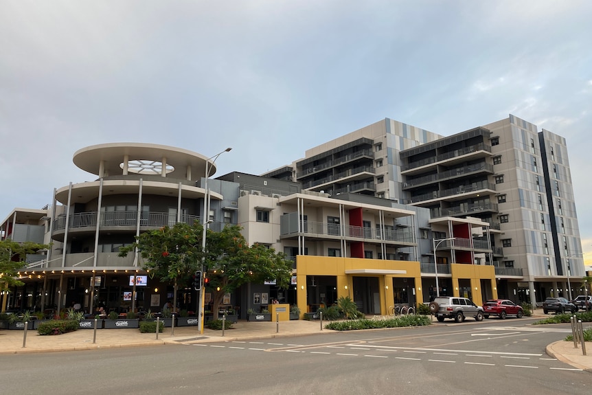 A low rise block of apartments with a round feature at the front stands in front of a taller block of apartments.