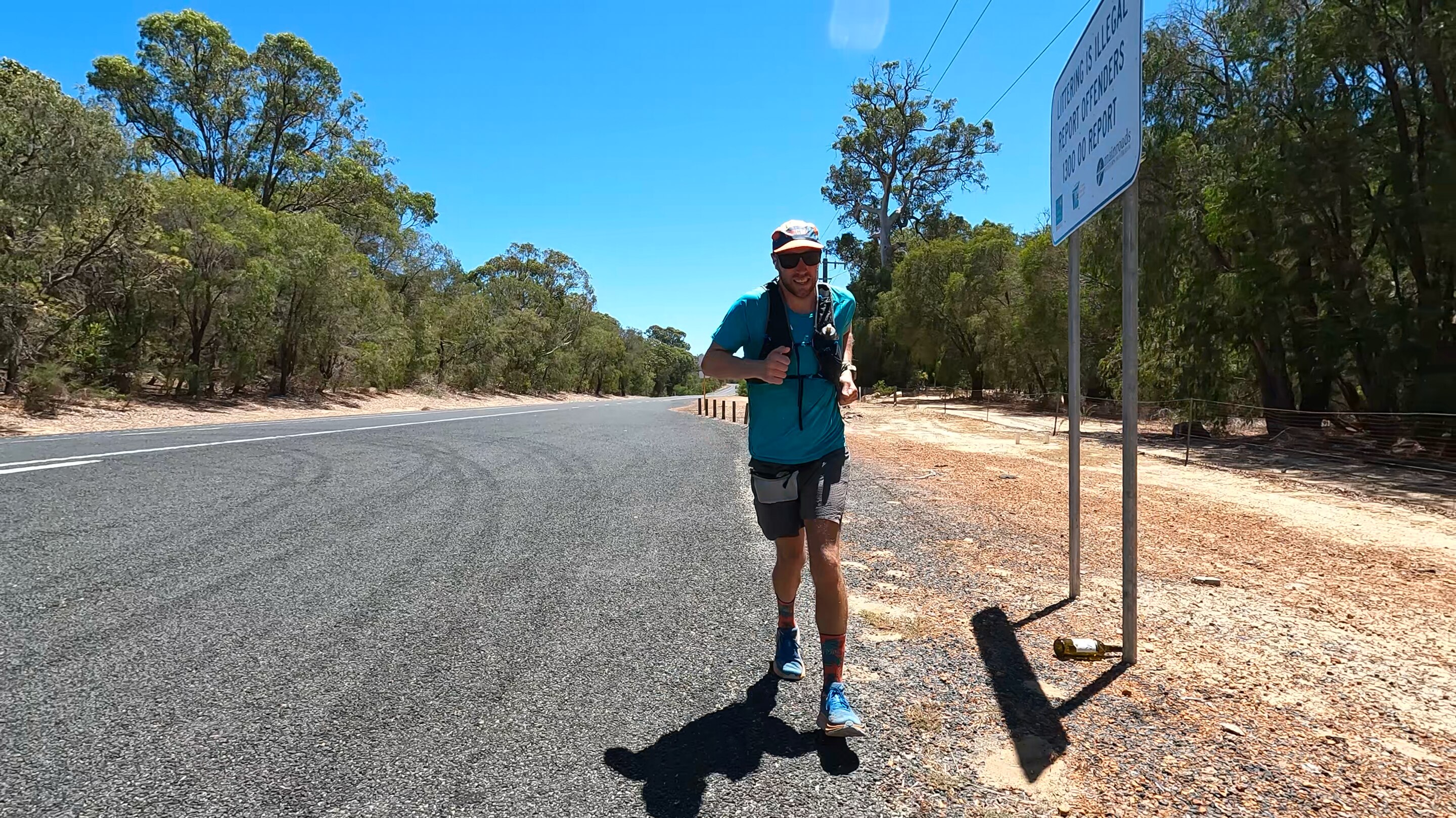 A man runs down a road in outback South West WA. The sky is blue and sun is beating down.