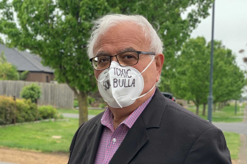 John Karagiannidis wearing a white mask puts an election leaflet into a post box.