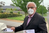 John Karagiannidis wearing a white mask puts an election leaflet into a post box.