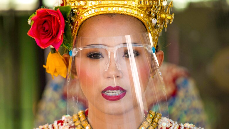 A woman in a Thai traditional outfit wearing a clear face shield