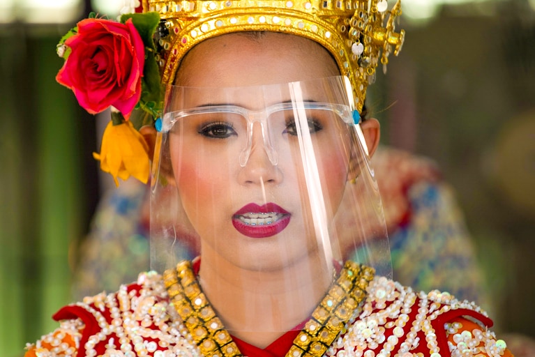A woman in a traditional Thai outfit wearing a clear face shield