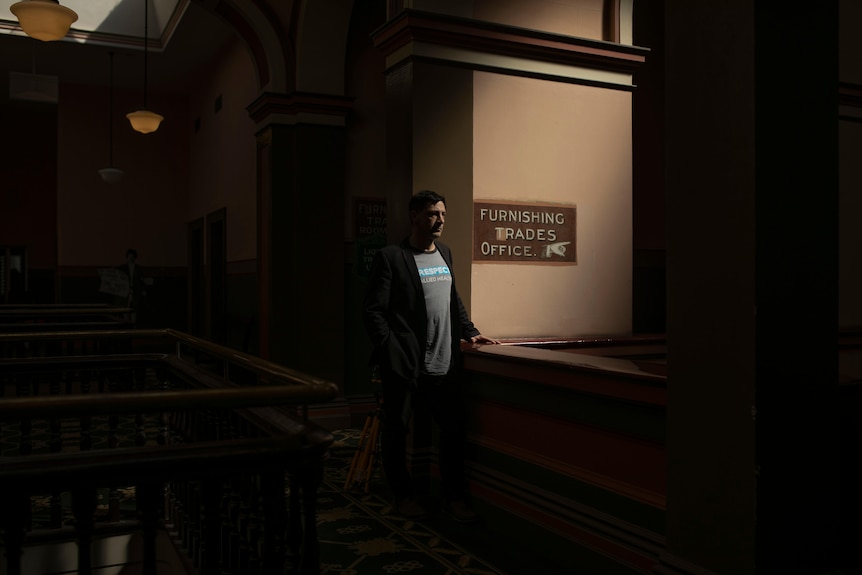 a man stands in melbourne union hall next to a sign that says furnishing trades office