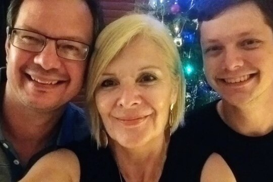 A woman standing taking a selfie between her two adult sons