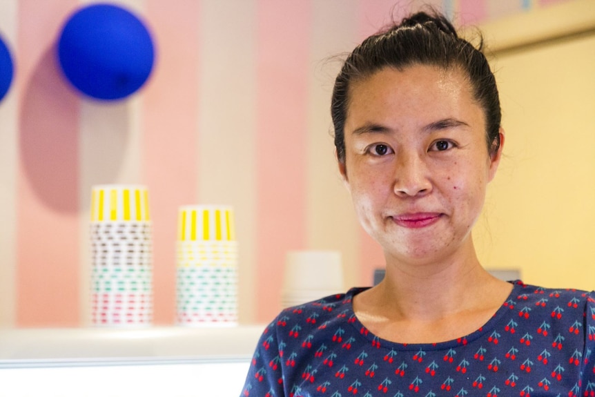 Susan Hhi stands smiling inside her brightly painted ice-cream store