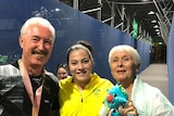Three people smile and pose with a medal