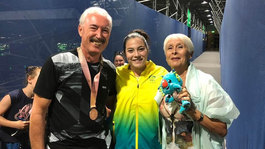 Three people smile and pose with a medal