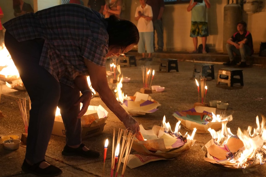 Senior Chinese woman leaning in to burn joss paper.