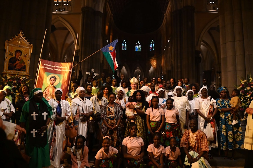 A group of people, most of whom are Black, stand smiling in a posed photo in a Catholic church.