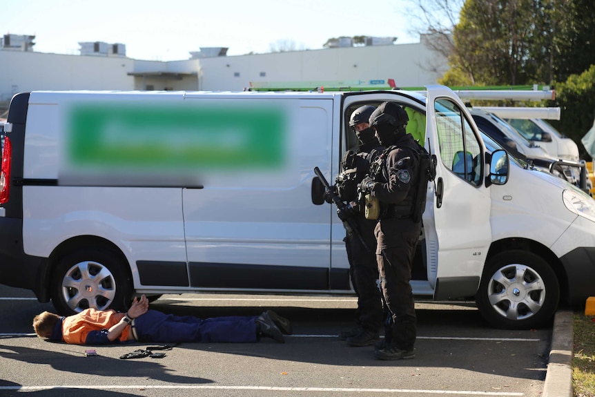 A man lies on the ground in handcuffs stood over by armed police