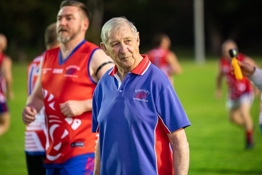 A mid shot of Kevin looking to the side with players out of focus on the field behind him 