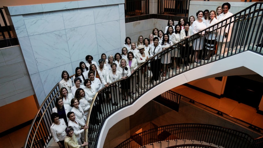 A group of women wearing white standing together while standing on the stairs.