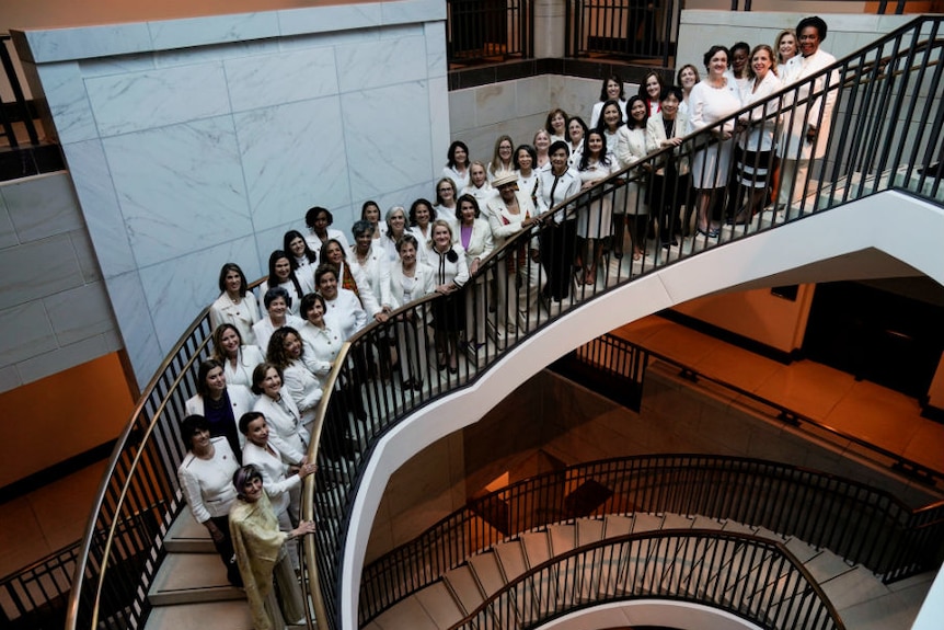 A group of women wearing white standing together while standing on the stairs.