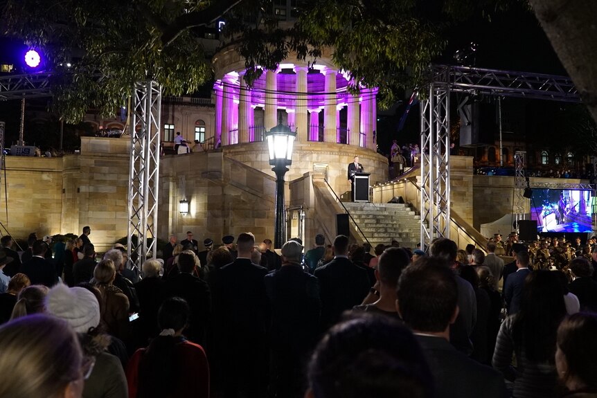 Purple light lights up ANZAC Square with a large crowd looking on.