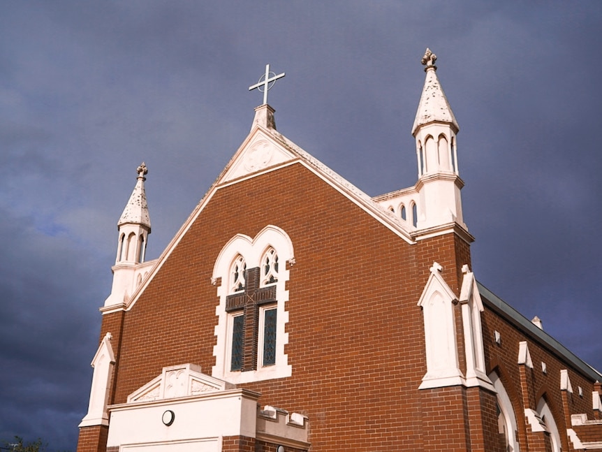 Image of a red brick catholic church with cloudy skies in the background