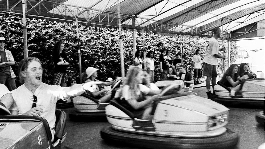 A black-and-white photo shows young people having fun on dodgem cars.