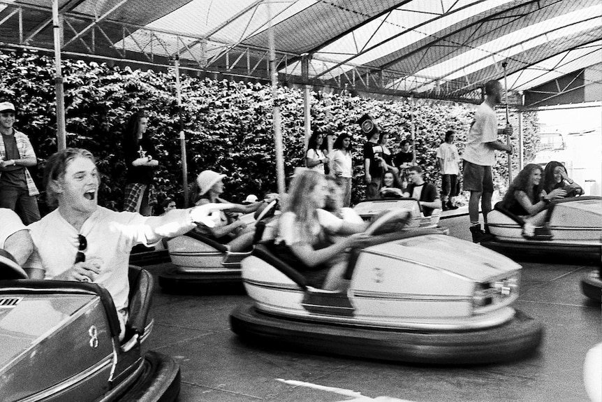 A black-and-white photo shows young people having fun on dodgem cars.