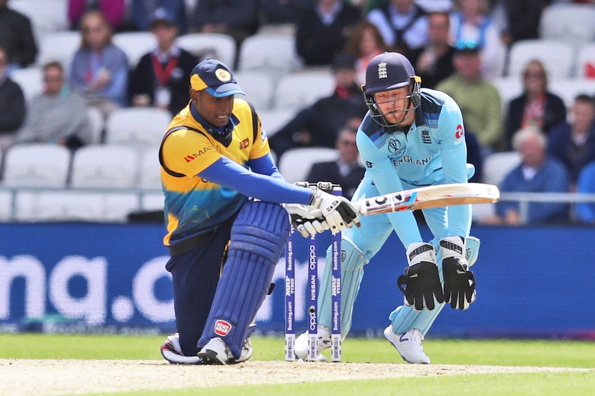 A batsman swings at the ball while a wicketkeeper braces behind the stumps.