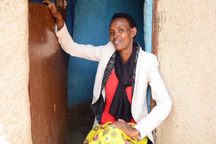 An African woman sits down with her hand on her knee at her front door.