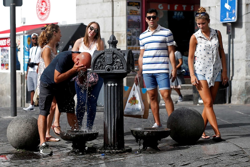 A tourist drinks water from a public fountain in Madrid