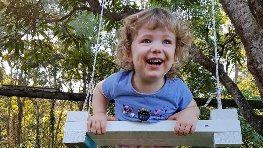 A young girl leans over a tree swing, smiling.