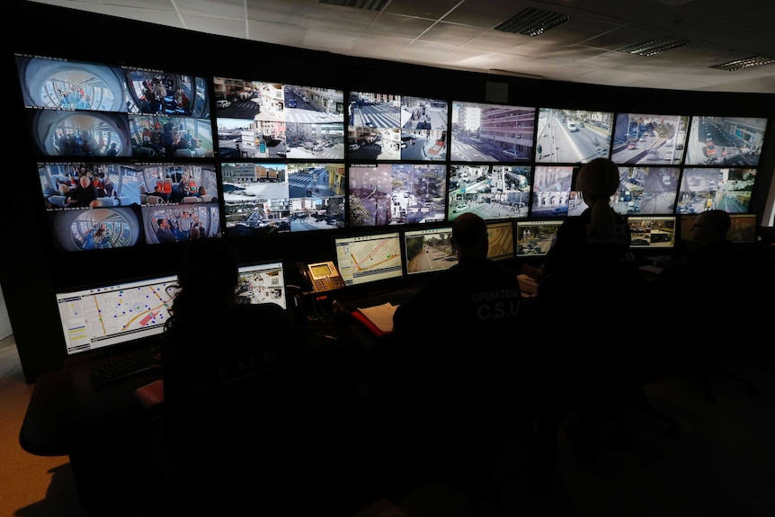 Inside a darkened room are dozens of screens showing images from surveillance cameras.