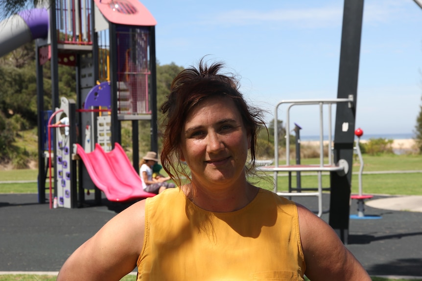 A woman in a yellow short sleeved top stands in a children's playground