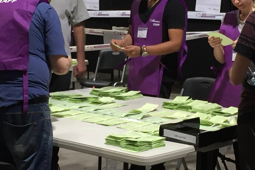 Two AEC staff count votes with ballots piled up on a table.