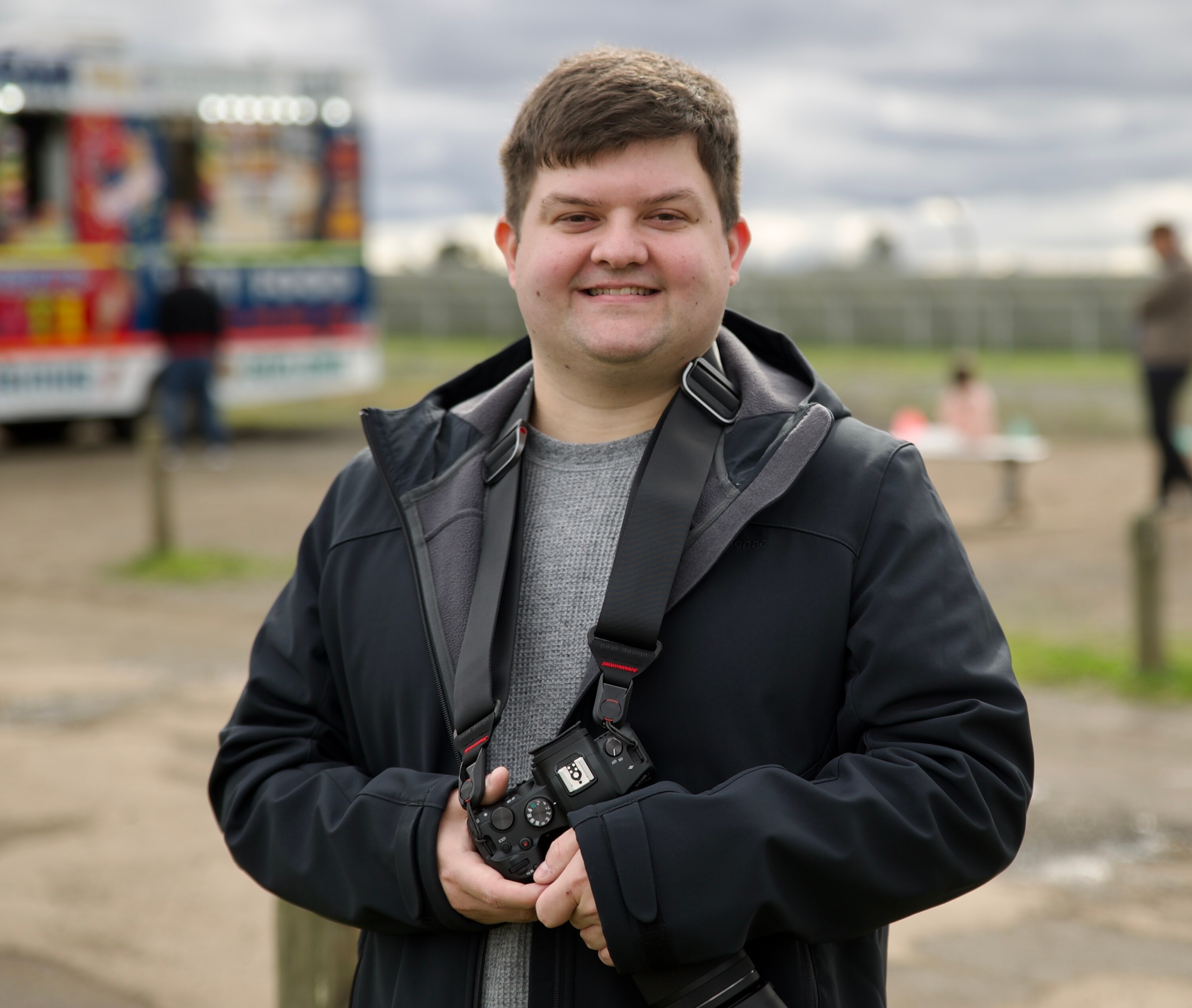 A man in a black jacket who is smiling.  He is holding a camera.
