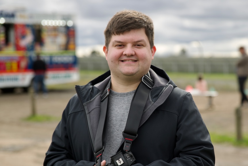 A man in a black jacket who is smiling. He is holding a camera.