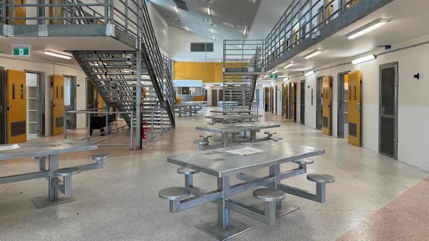 Metal picnic tables in the middle of a room lined with prison cells.