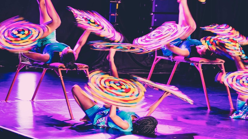 circus performers lying on their back twirling colourful batons on their feet and hands.