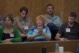 Five people sitting in the jury dock, an old woman in a tie dye tshirt at the centre clapping