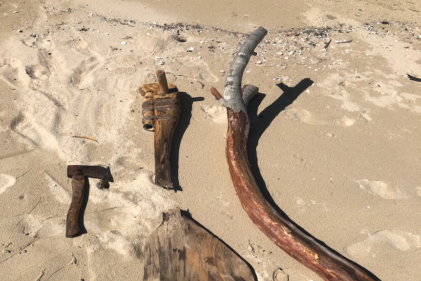a broken oar, a long stick and a hammer laid out on a sand bank