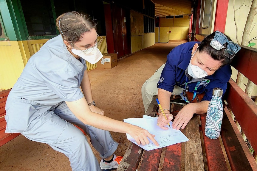 Two health workers in full PPE pour over a document. They are at a health clinic.