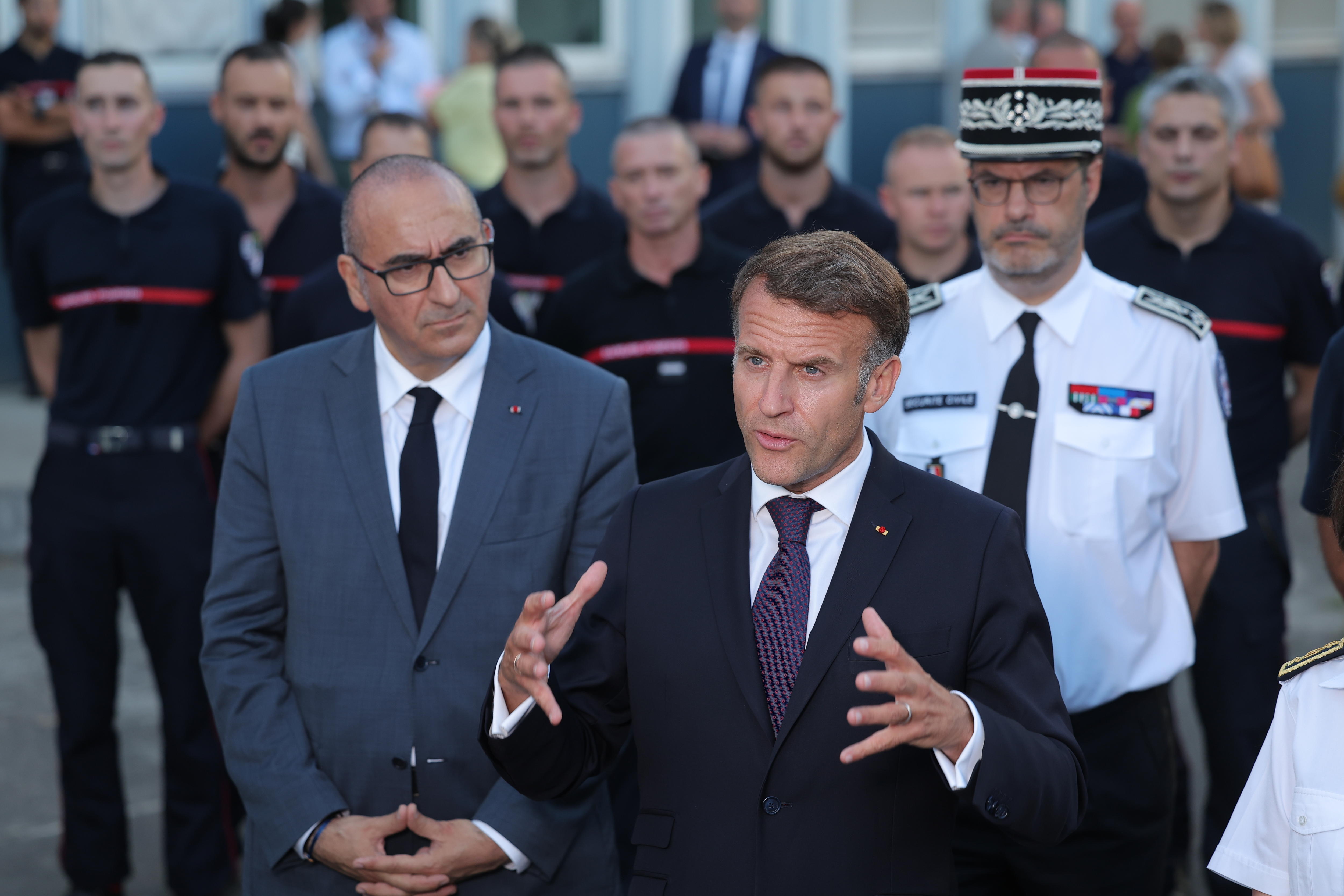 A man in a dark suit — French President Emmanuel Macron — gestures as he speaks while others watch on.