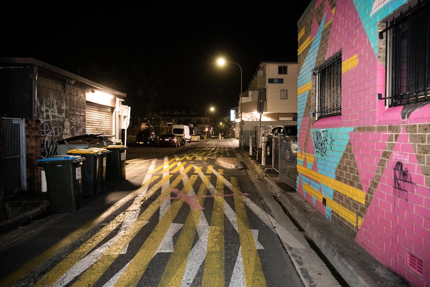 A side street at night with white and yellow lines on the floor and a brick building painted brick.