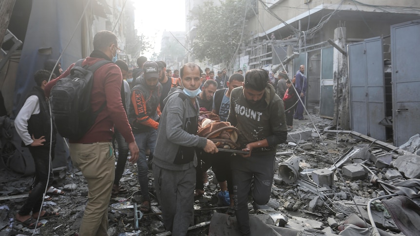 people carry someone on a stretcher while stepping through debris