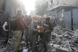 people carry someone on a stretcher while stepping through debris