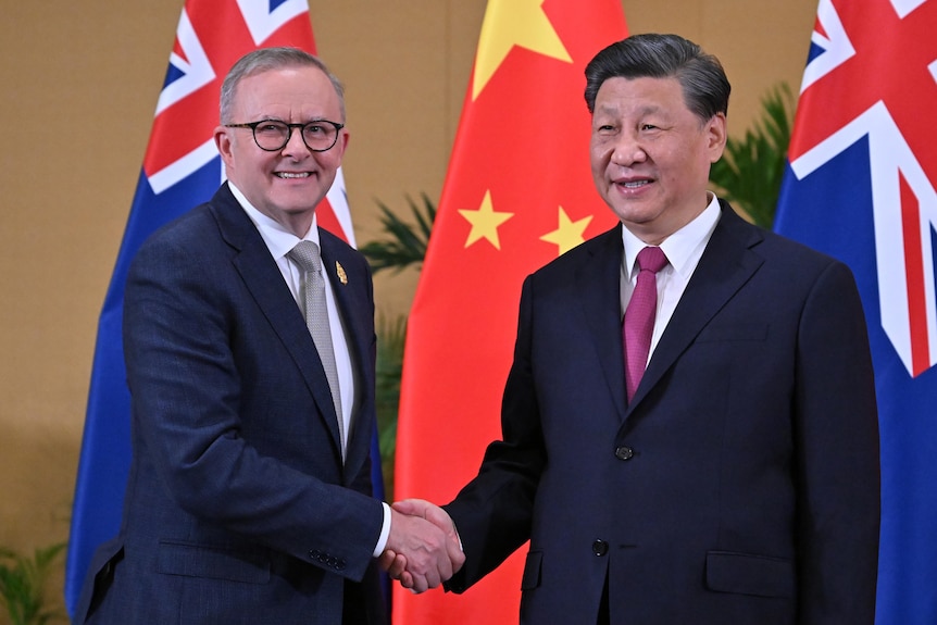 Энтони Альбанезе и Си Цзиньпин обмениваются рукопожатием перед флагами Китая и Австралии.
