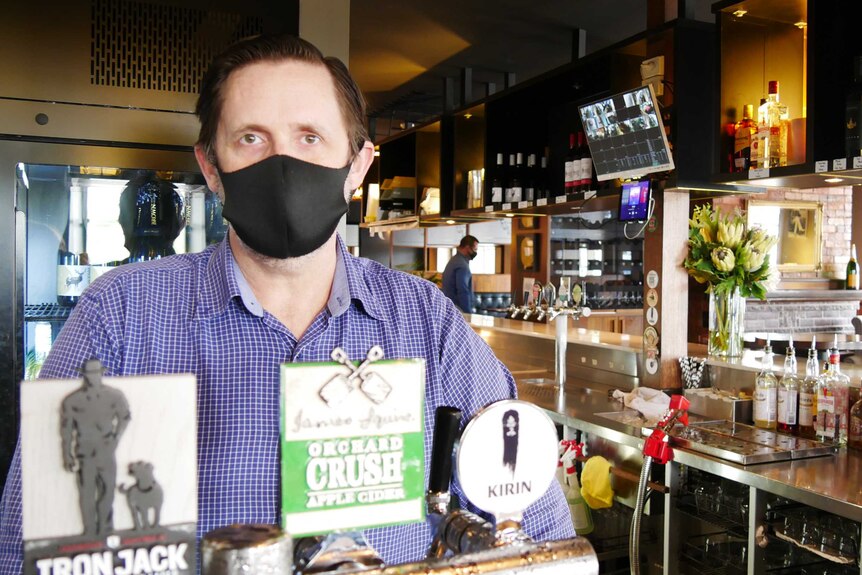 A man wearing a face stands behind a bar in a pub.