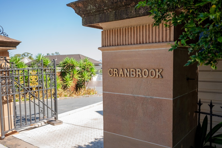 A stone pillar with the word 'CRANBROOK' in gold and an open gate
