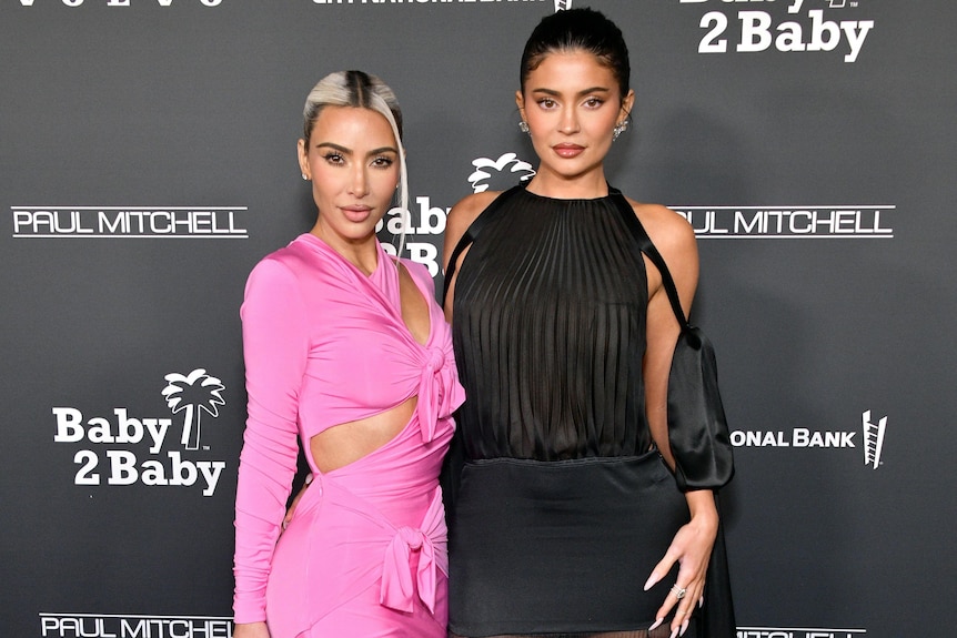 Woman in pink dress next to woman in black dress, both posing at red carpet event.