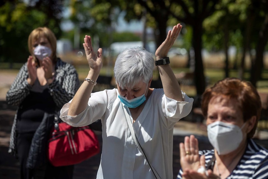 three women in masks hold up their hands outside