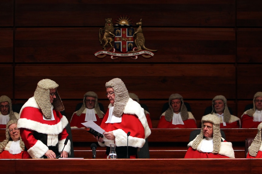 men in court wearing wigs watching as two men stand up one reading in front of other man
