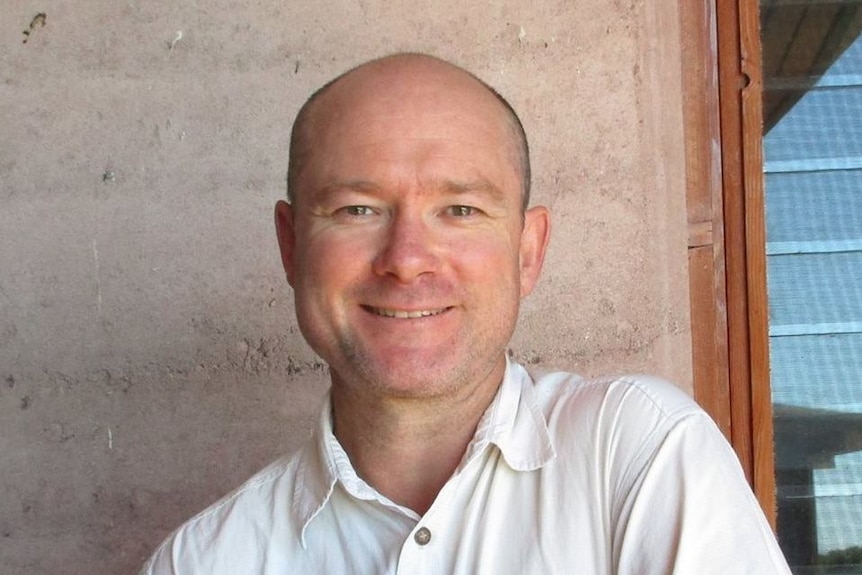 A headshot of a bald man in a white shirt.