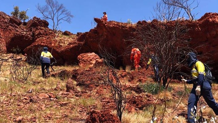 emergency workers searching among red rock crevices in the Pilbara.